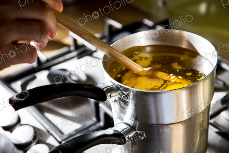 High angle close up of person melting wax for candles in saucepan on stove.