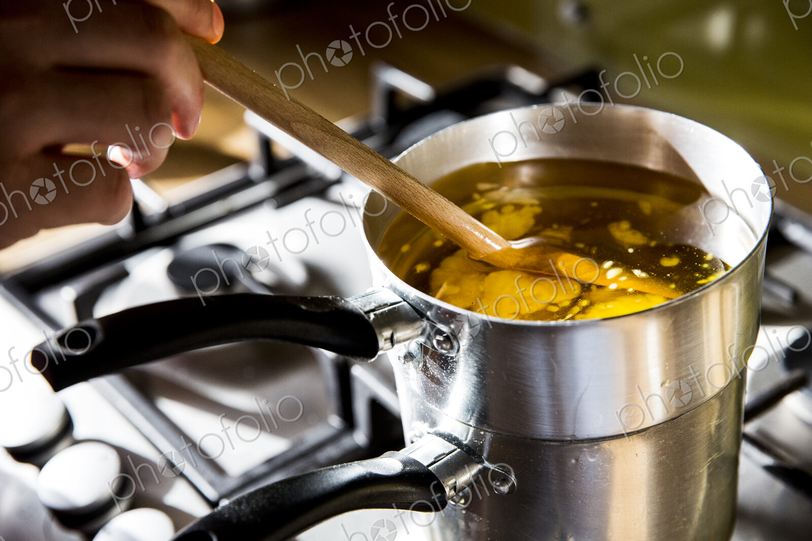 High angle close up of person melting wax for candles in saucepan on stove.