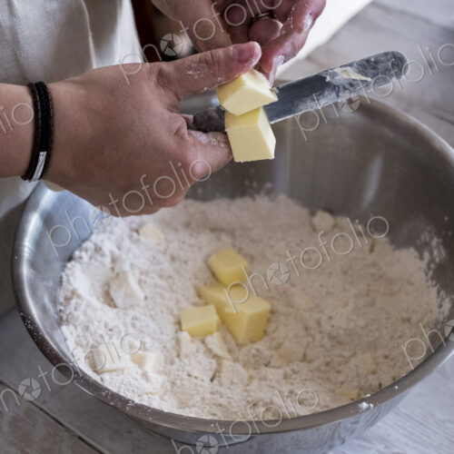 High angle close up of person mixing butter and flour for a crumble in metal bowl.