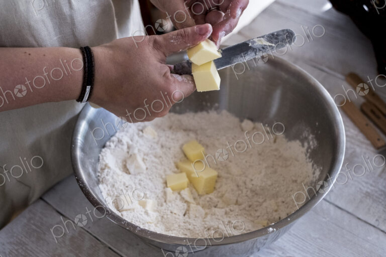 High angle close up of person mixing butter and flour for a crumble in metal bowl.