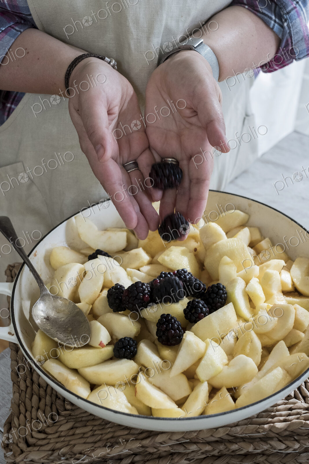 High angle close up of person placing apples and blackberries in a round baking tin.