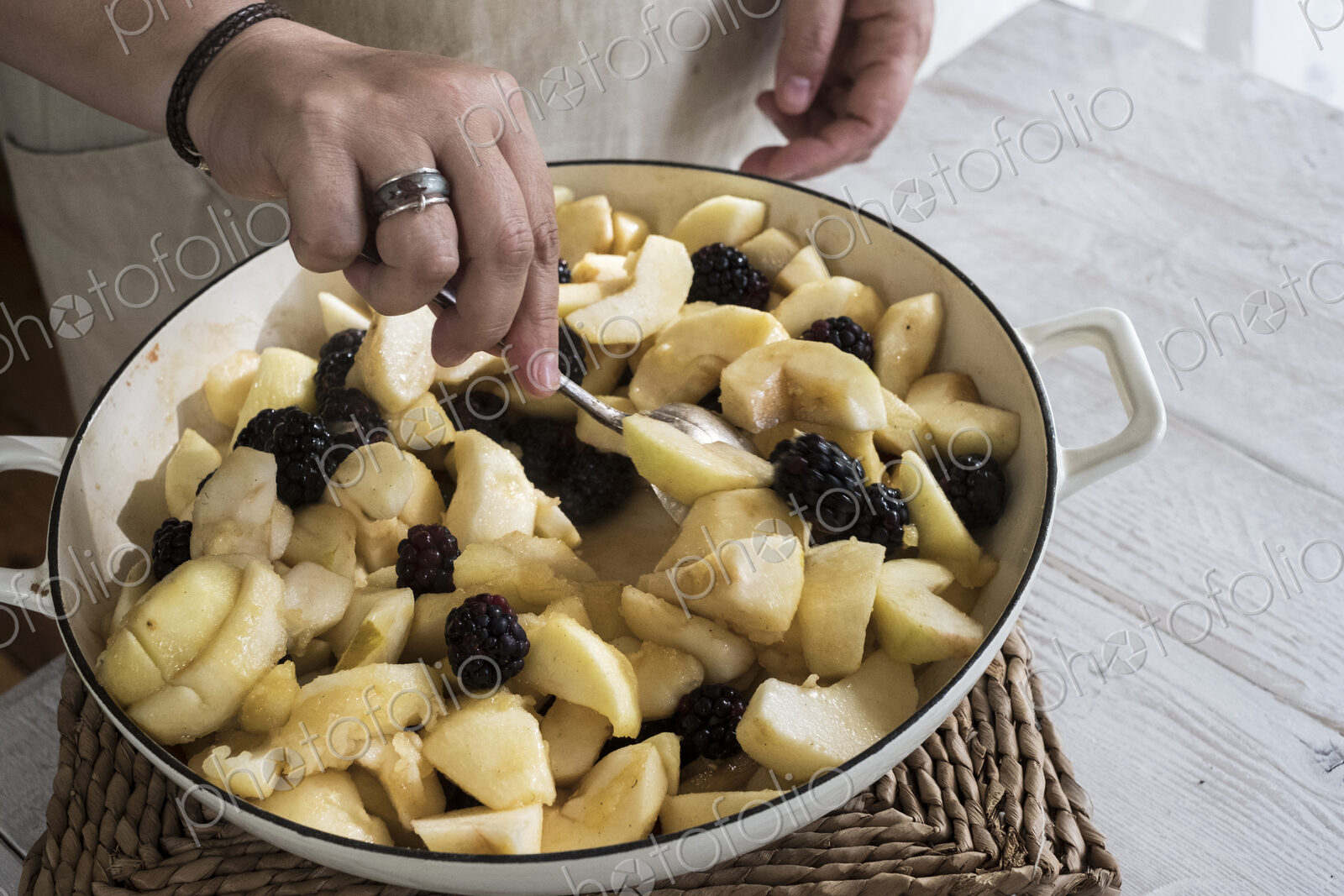 High angle close up of person placing apples and blackberries in a round baking tin.