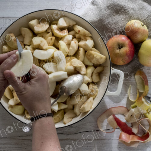 High angle close up of person placing apples in a round baking tin.