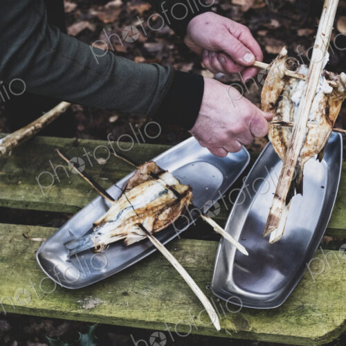 High angle close up of person placing grilled fish on wooden skewers on metal plates,…