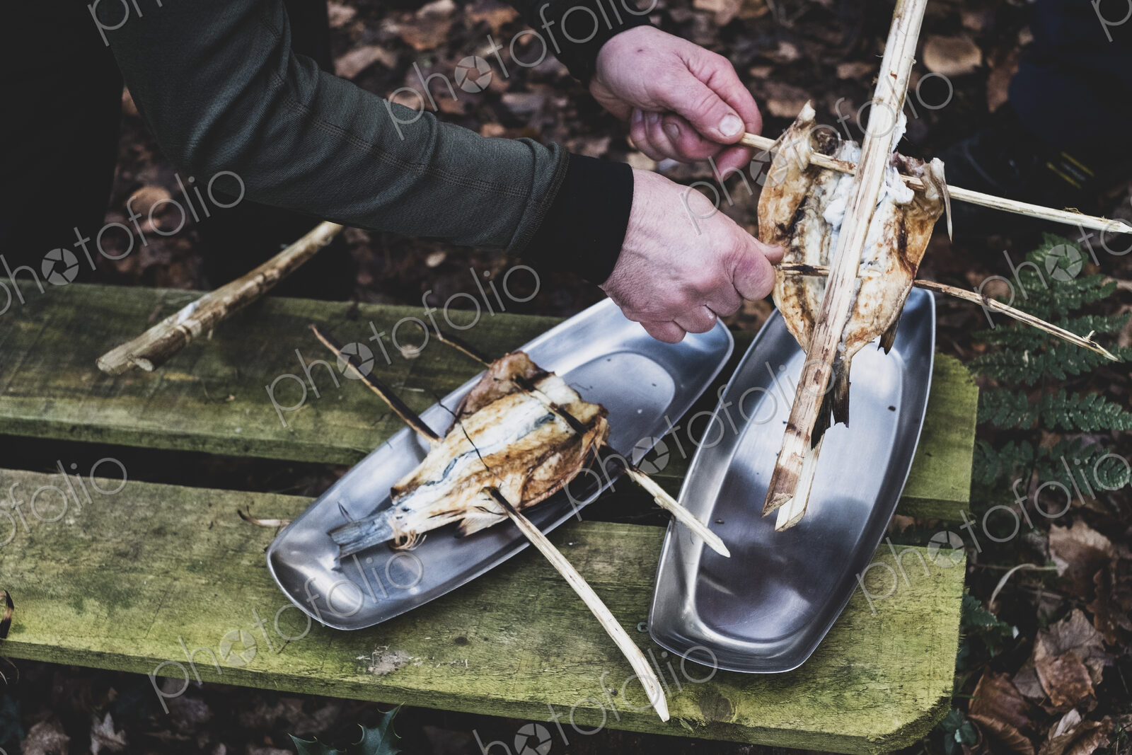 High angle close up of person placing grilled fish on wooden skewers on metal plates,…