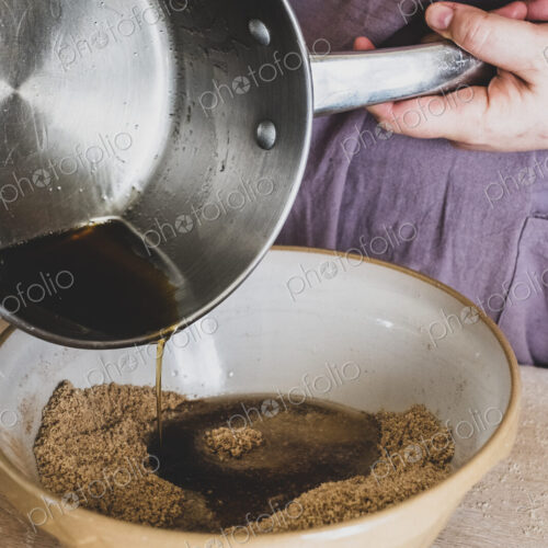 High angle close up of person pouring liquid into mixing bowl with baking ingredients.