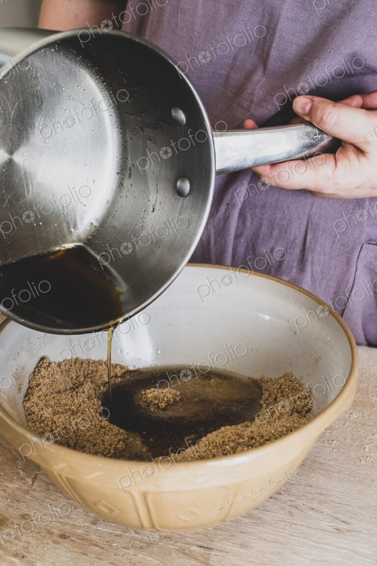High angle close up of person pouring liquid into mixing bowl with baking ingredients.