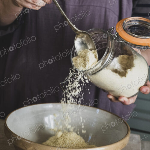 High angle close up of person pouring sugar into mixing bowl with baking ingredients.