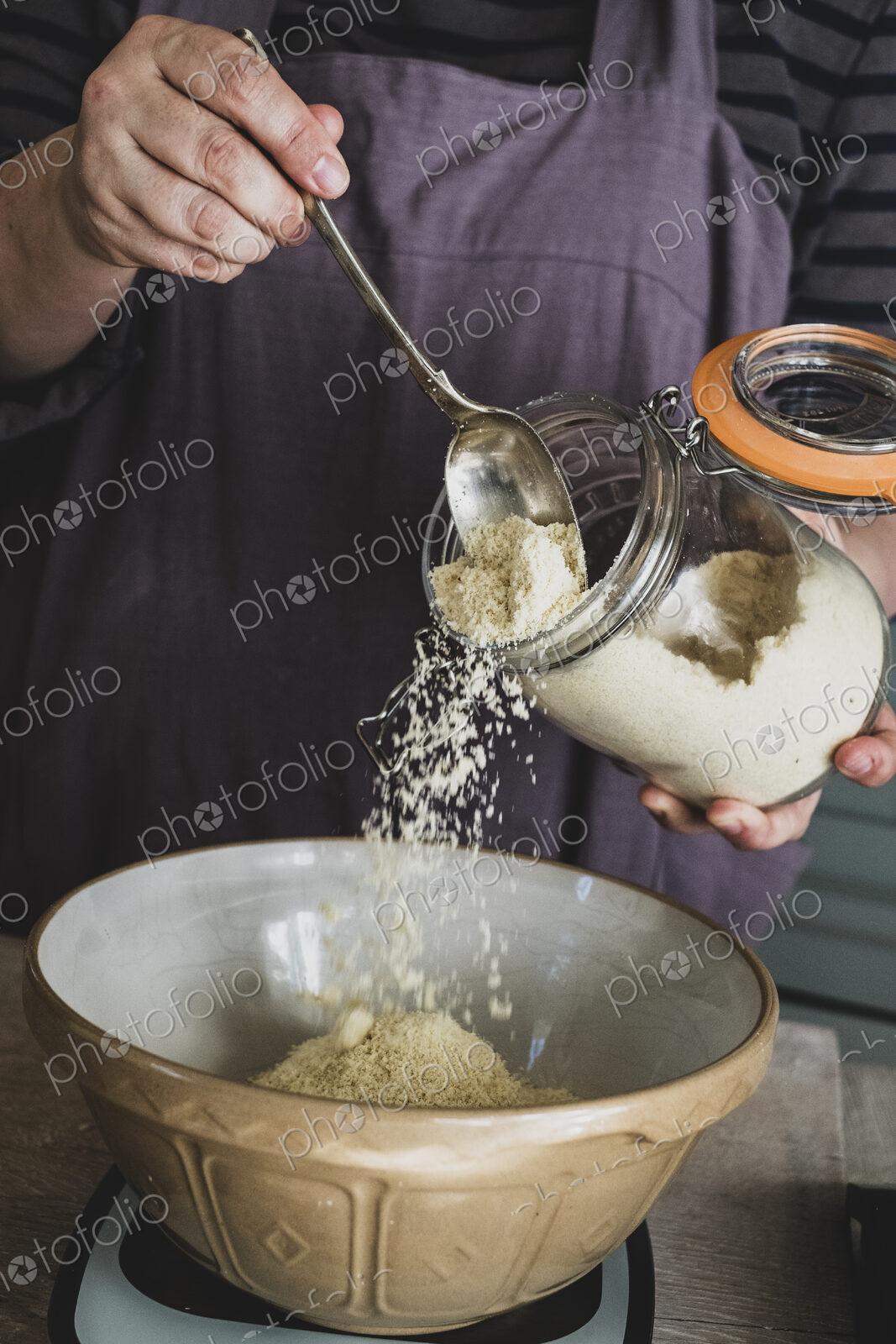 High angle close up of person pouring sugar into mixing bowl with baking ingredients.