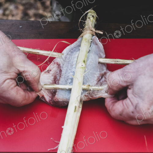 High angle close up of person preparing fish on wooden skewers for grilling.