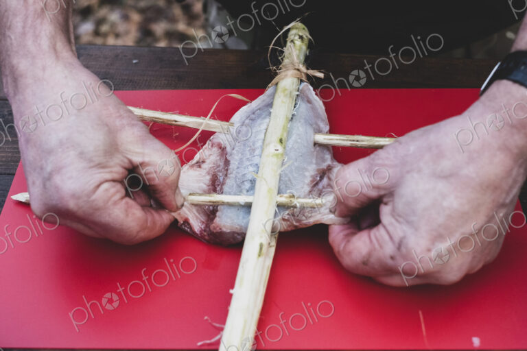 High angle close up of person preparing fish on wooden skewers for grilling.