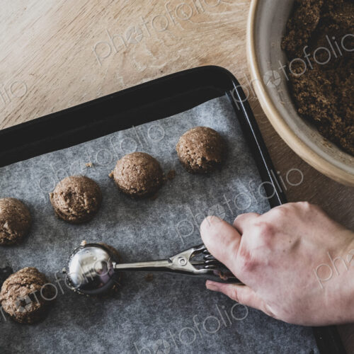High angle close up of person putting chocolate cookie dough on a baking tray. High angle close up of person putting chocolate cookie dough on a baking tray.