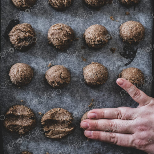 High angle close up of person putting chocolate cookie dough on a baking tray. High angle close up of person putting chocolate cookie dough on a baking tray.