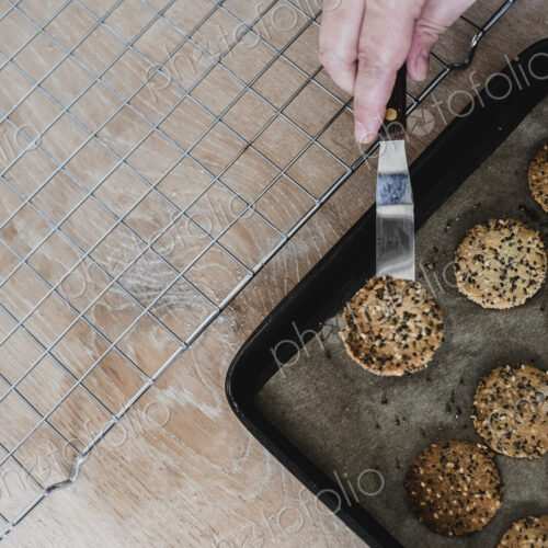 High angle close up of person removing freshly baked seeded crackers from a baking tray. High angle close up of person removing freshly baked seeded crackers from a baking tray.