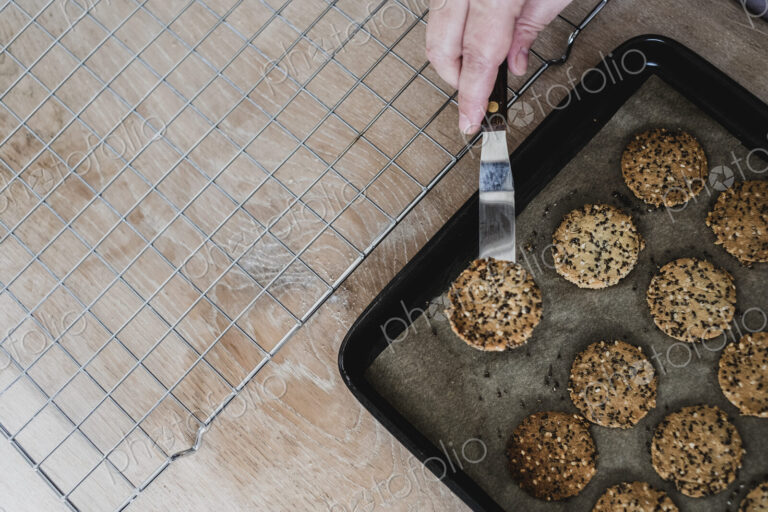 High angle close up of person removing freshly baked seeded crackers from a baking tray.