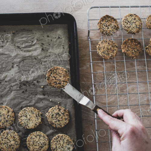 High angle close up of person removing freshly baked seeded crackers from a baking tray. High angle close up of person removing freshly baked seeded crackers from a baking tray.