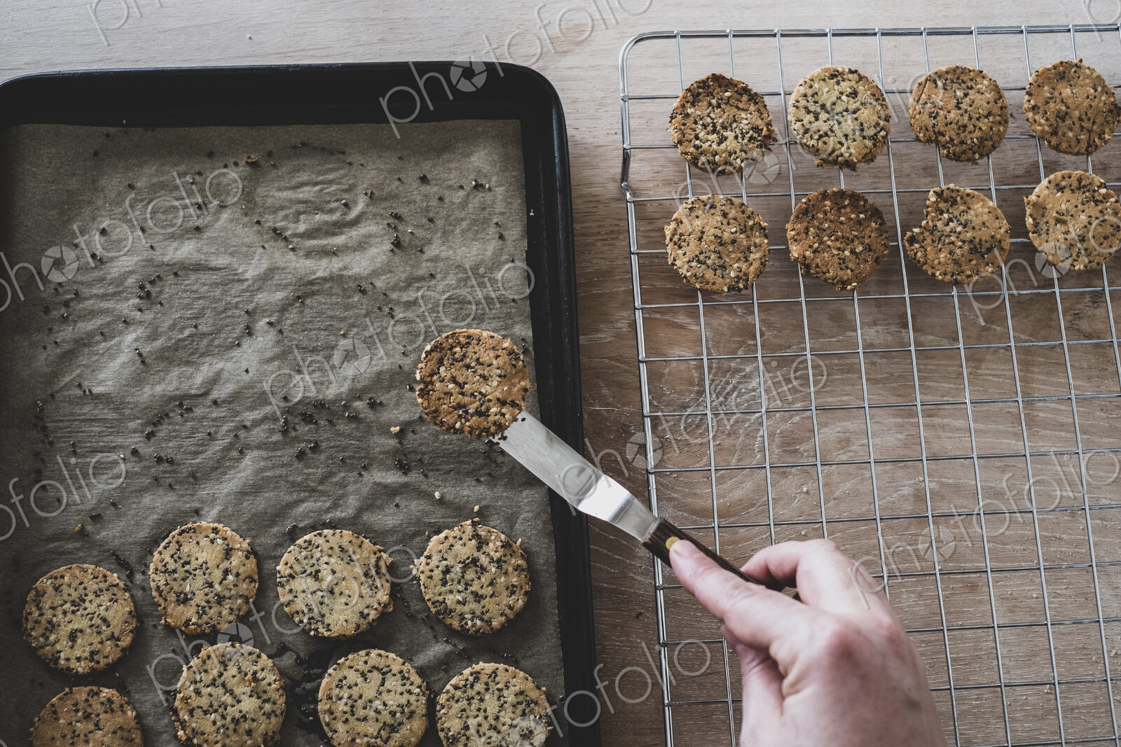 High angle close up of person removing freshly baked seeded crackers from a baking tray.