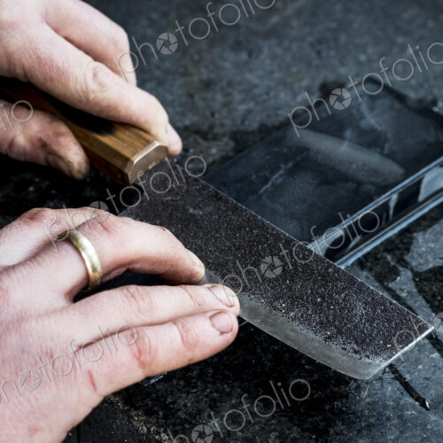 High angle close up of person sharpening handmade knife on a whetstone. High angle close up of person sharpening handmade knife on a whetstone.