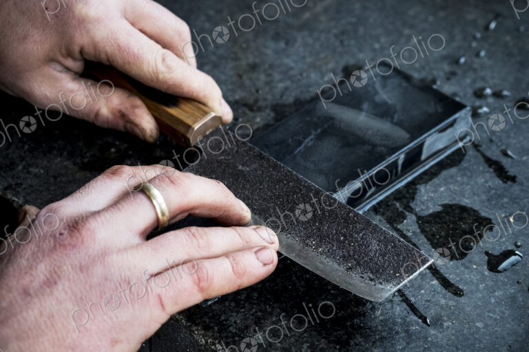 High angle close up of person sharpening handmade knife on a whetstone.