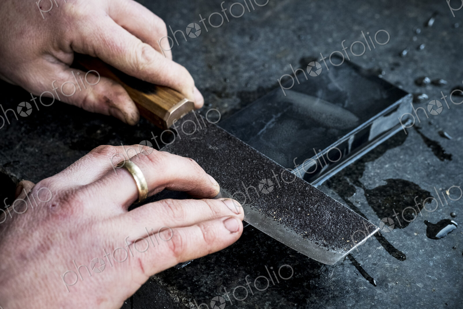 High angle close up of person sharpening handmade knife on a whetstone.