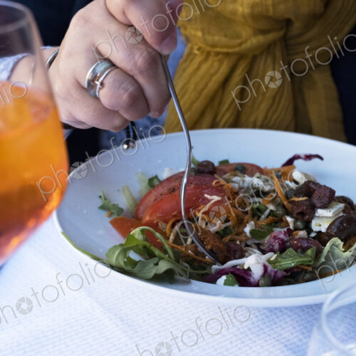 High angle close up of person sitting at a table, eating mixed salad and a glass of…