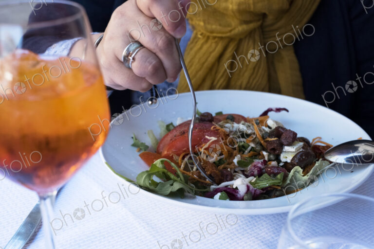 High angle close up of person sitting at a table, eating mixed salad and a glass of…