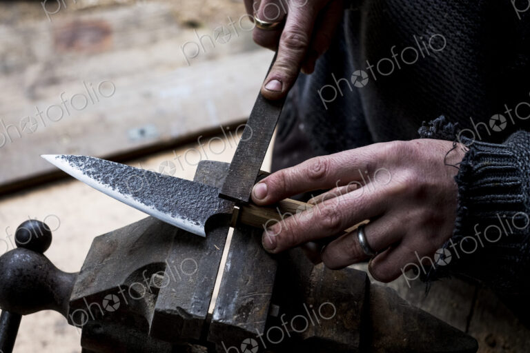 High angle close up of person working on handmade knife using a file.