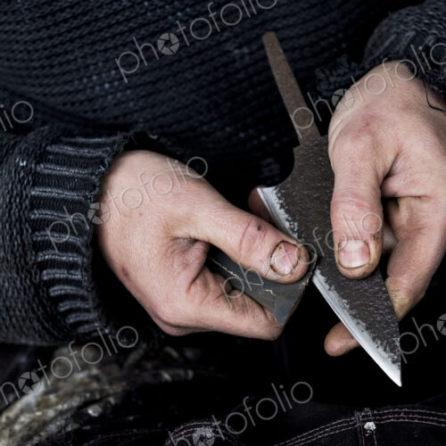 High angle close up of person working on handmade knife using piece of sandpaper. High angle close up of person working on handmade knife using piece of sandpaper.