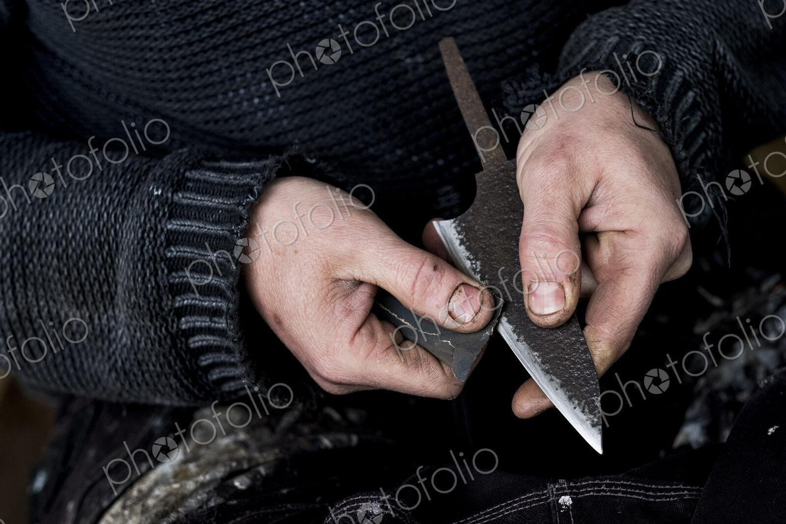 High angle close up of person working on handmade knife using piece of sandpaper.