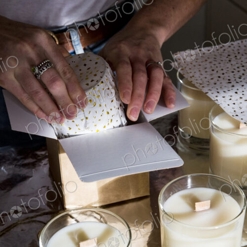 High angle close up of person wrapping handmade white jar candles. High angle close up of person wrapping handmade white jar candles.