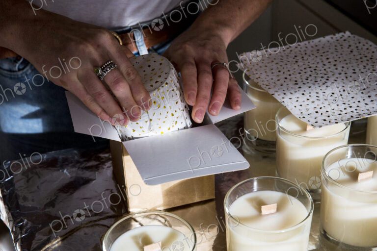 High angle close up of person wrapping handmade white jar candles.