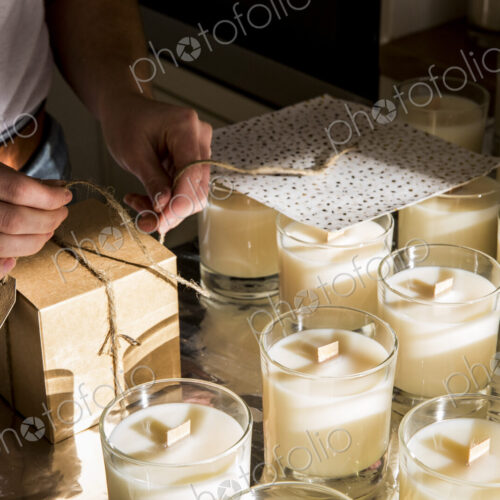 High angle close up of person wrapping handmade white jar candles. High angle close up of person wrapping handmade white jar candles.