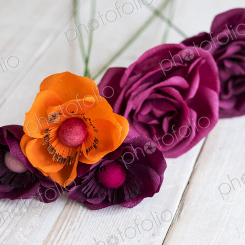 High angle close up of pink and purple paper roses and an orange poppy. High angle close up of pink and purple paper roses and an orange poppy.
