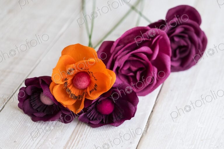 High angle close up of pink and purple paper roses and an orange poppy.