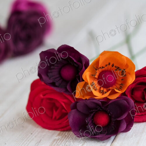 High angle close up of red and purple paper roses and an orange poppy. High angle close up of red and purple paper roses and an orange poppy.