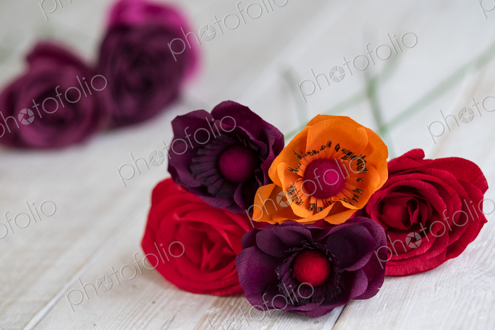 High angle close up of red and purple paper roses and an orange poppy.