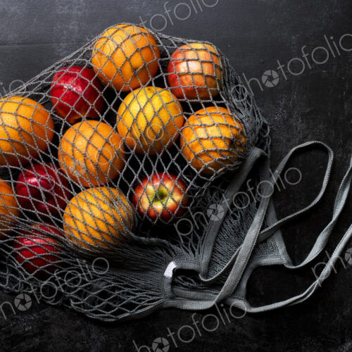 High angle close up of red apples and oranges in grey net bag on black background. High angle close up of red apples and oranges in grey net bag on black background.