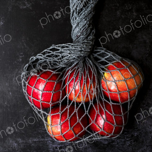 High angle close up of red apples in grey net bag on black background. High angle close up of red apples in grey net bag on black background.