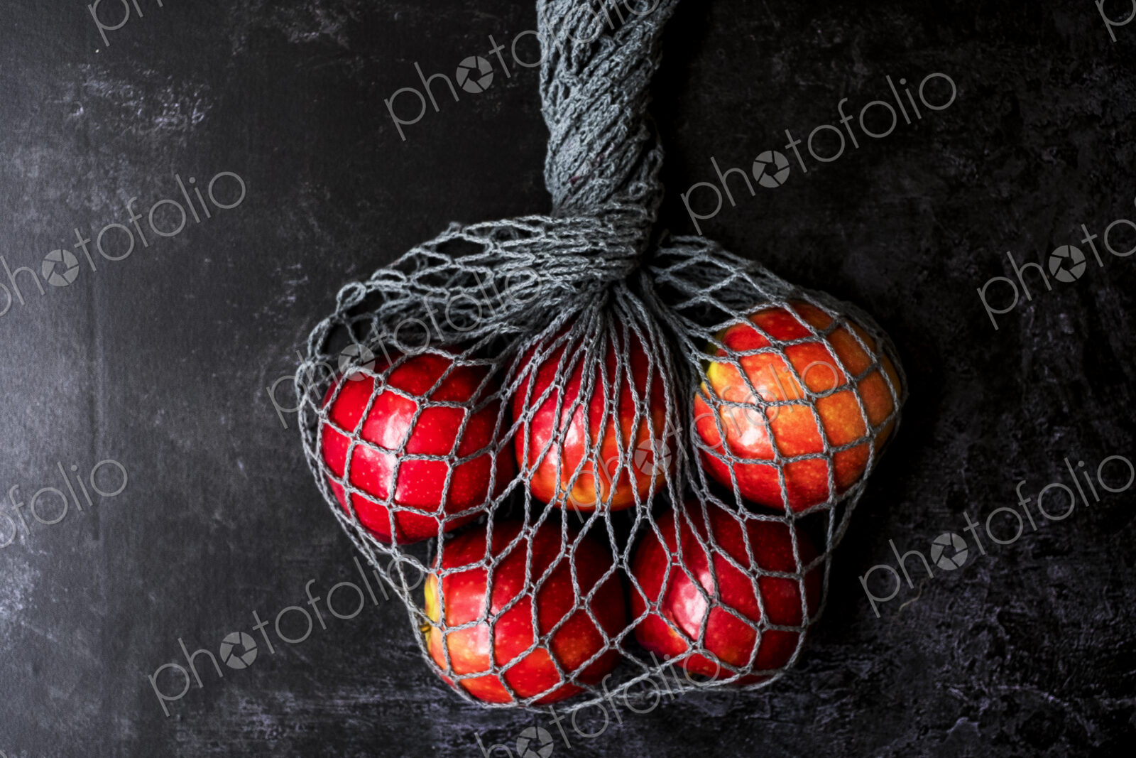 High angle close up of red apples in grey net bag on black background.