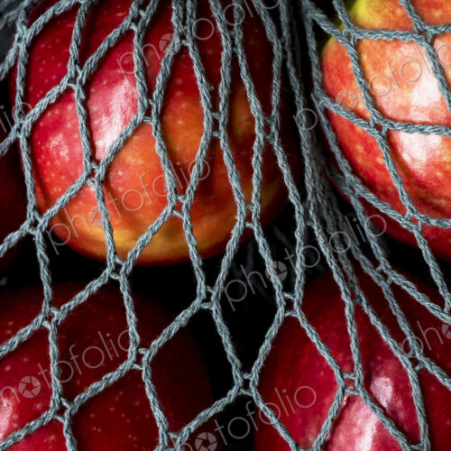 High angle close up of red apples in grey net bag on black background. High angle close up of red apples in grey net bag on black background.