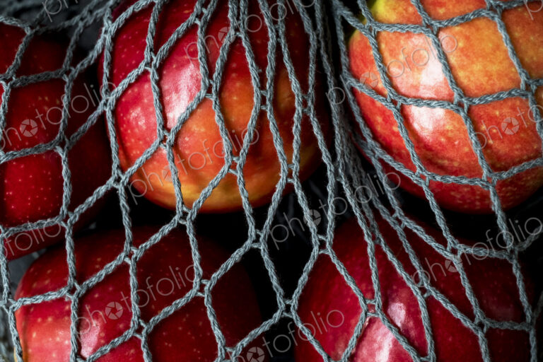 High angle close up of red apples in grey net bag on black background.