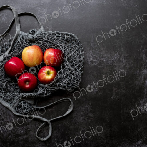 High angle close up of red apples in grey net bag on black background. High angle close up of red apples in grey net bag on black background.