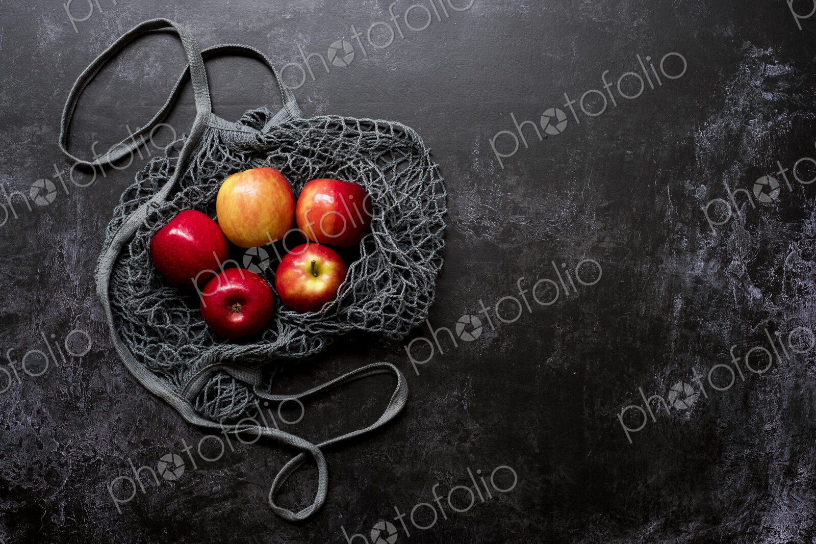 High angle close up of red apples in grey net bag on black background.