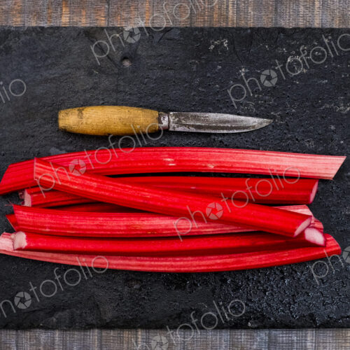 High angle close up of rhubarb stalks and knife on black slate. High angle close up of rhubarb stalks and knife on black slate.