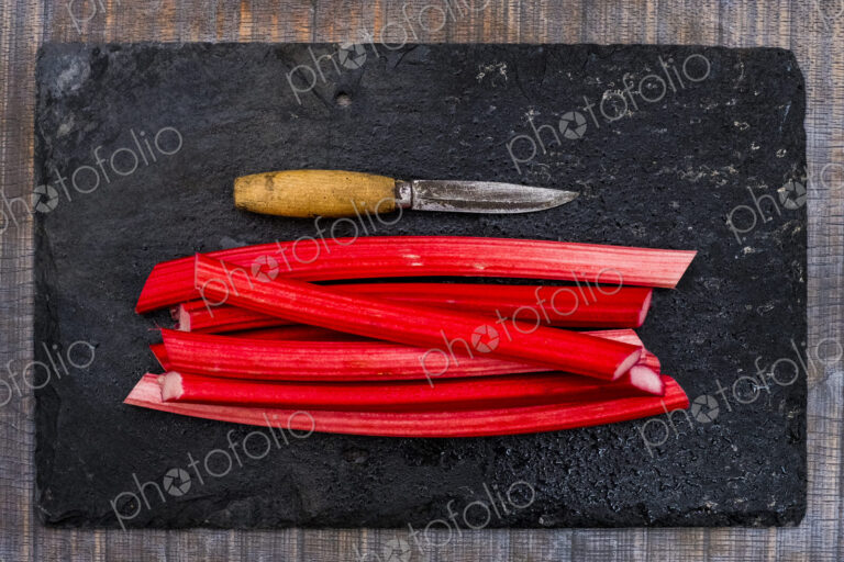 High angle close up of rhubarb stalks and knife on black slate.