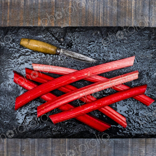 High angle close up of rhubarb stalks and knife on black slate. High angle close up of rhubarb stalks and knife on black slate.