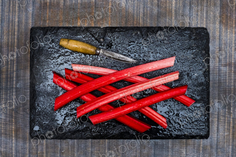 High angle close up of rhubarb stalks and knife on black slate.