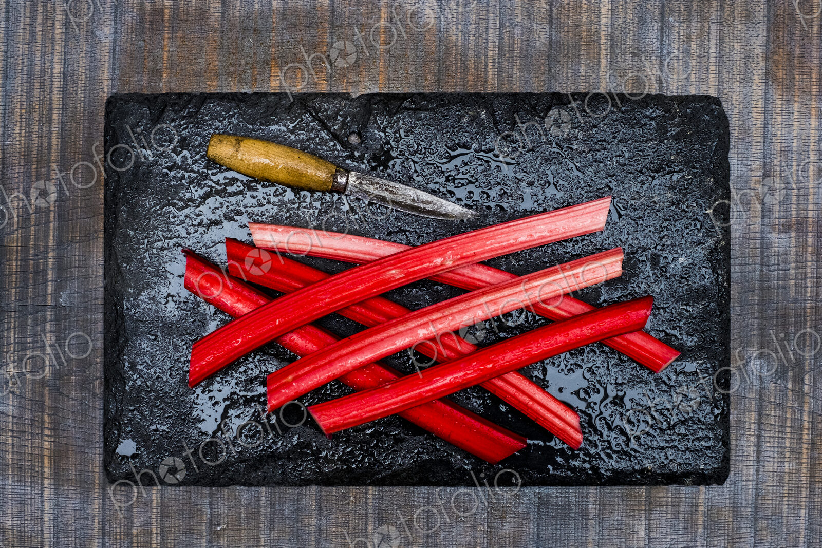 High angle close up of rhubarb stalks and knife on black slate.