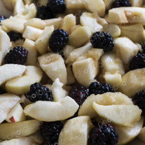 High angle close up of round baking tin with apples and blackberries.