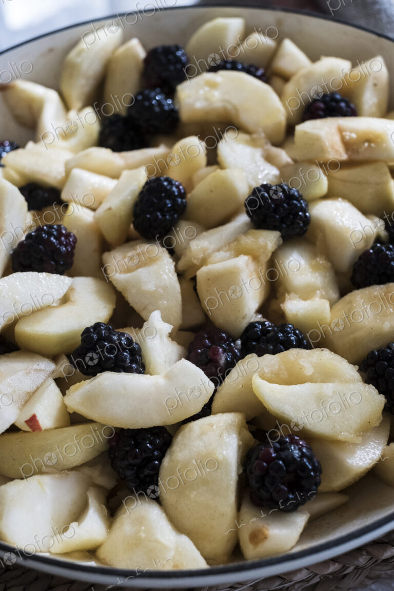 High angle close up of round baking tin with apples and blackberries.